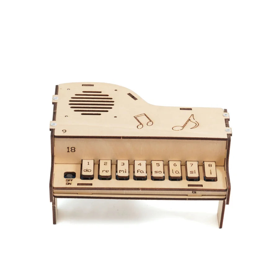 A partially assembled wooden electronic piano showing the internal circuitry, speaker, and wooden keys, emphasizing its educational and DIY nature.