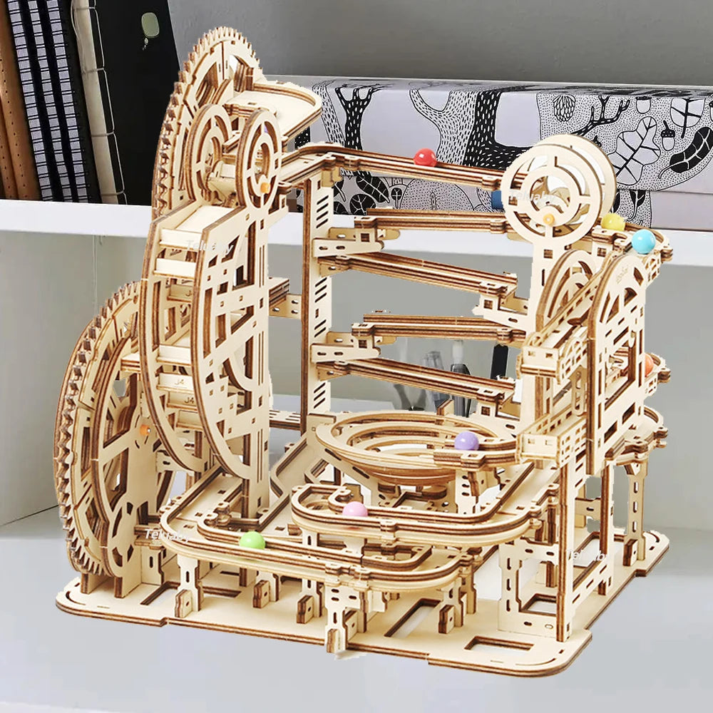 Two versions of Chriyungel mechanical marble runs: a large complex tower and a compact desktop version, both made of laser-cut wood with steel marbles.