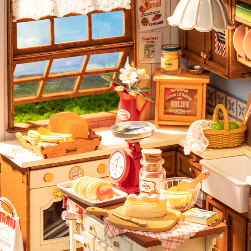 A fully assembled Rolife Baking Kitchen miniature house showing a vintage yellow chair, open oven with bread, and a glowing floral pendant lamp.