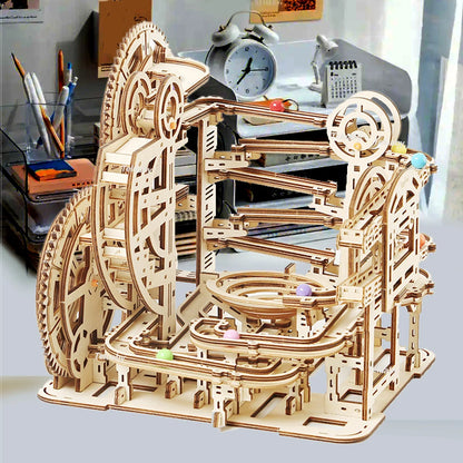 Two versions of Chriyungel mechanical marble runs: a large complex tower and a compact desktop version, both made of laser-cut wood with steel marbles.