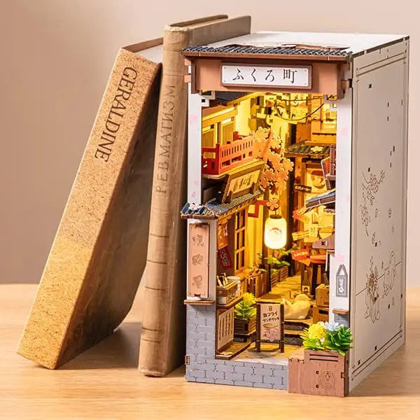 A completed Robotime Sakura Wine Alley Book Nook glowing with warm LED lights between books on a shelf, showing a detailed Japanese miniature street.