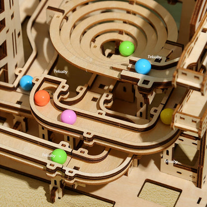 Two versions of Chriyungel mechanical marble runs: a large complex tower and a compact desktop version, both made of laser-cut wood with steel marbles.