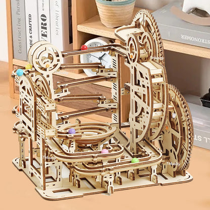 Two versions of Chriyungel mechanical marble runs: a large complex tower and a compact desktop version, both made of laser-cut wood with steel marbles.