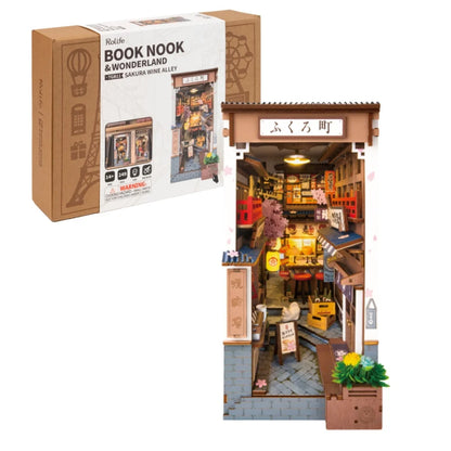 A completed Robotime Sakura Wine Alley Book Nook glowing with warm LED lights between books on a shelf, showing a detailed Japanese miniature street.